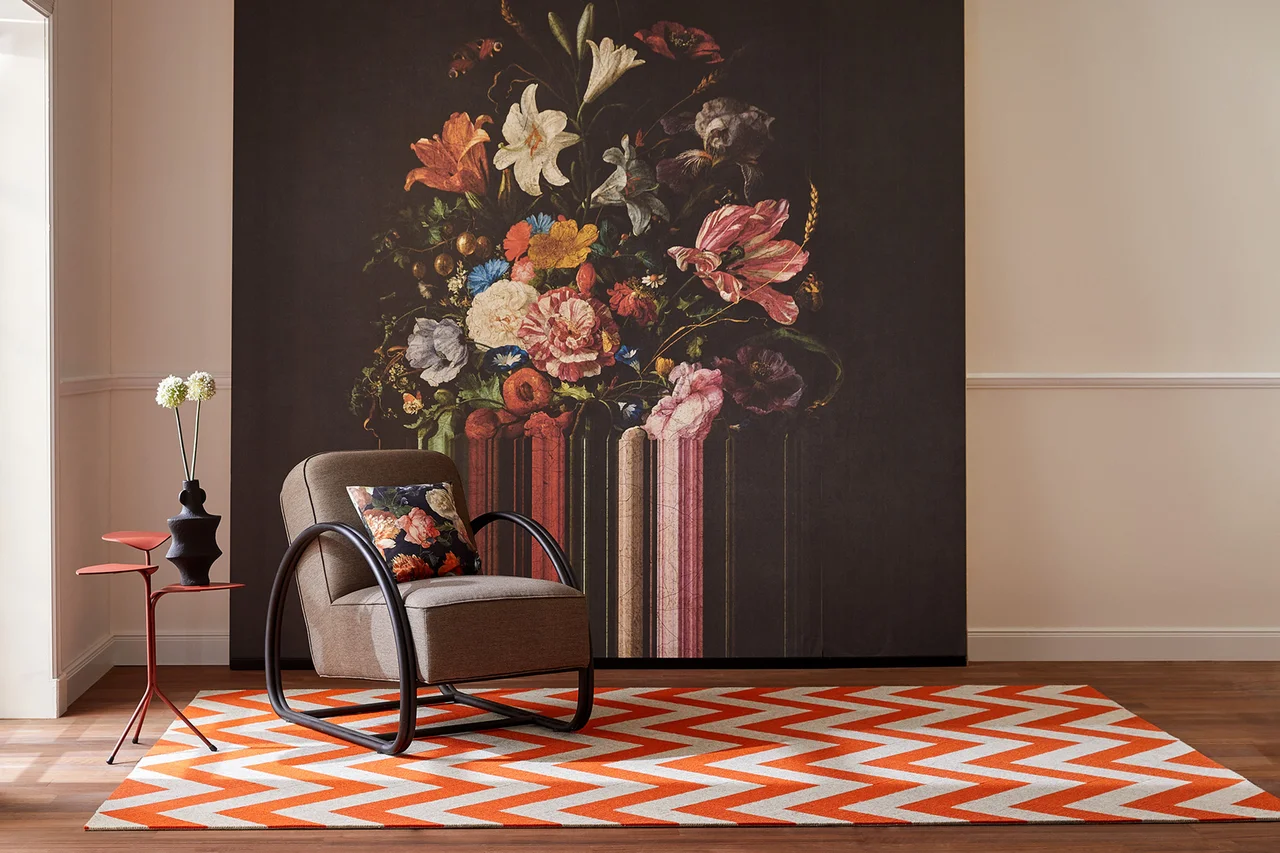 Illustration - Ihr Experte für schönes Wohnen - Ein orange beiger im Zickzack gemusterter Teppich liegt im Raum, im Hintergrund eine florale Tapete.